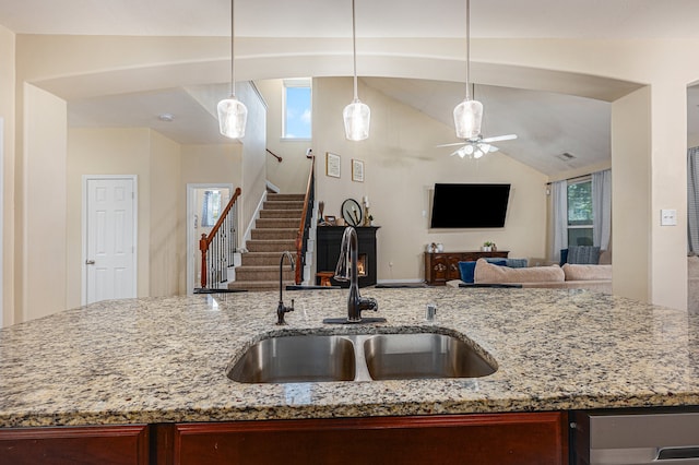 kitchen featuring lofted ceiling, ceiling fan, light stone counters, and sink