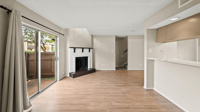 unfurnished living room featuring a textured ceiling, visible vents, a brick fireplace, stairs, and light wood-style floors