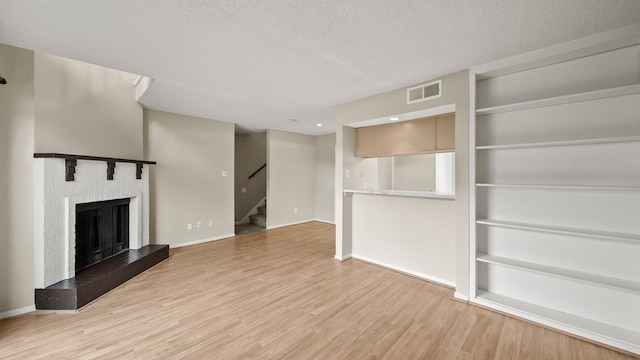 unfurnished living room featuring a textured ceiling, light wood-style flooring, visible vents, a fireplace, and stairway