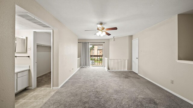unfurnished bedroom with light carpet, baseboards, a walk in closet, and a ceiling fan