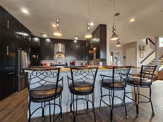 kitchen with kitchen peninsula, stainless steel fridge, wall chimney exhaust hood, pendant lighting, and dark hardwood / wood-style floors