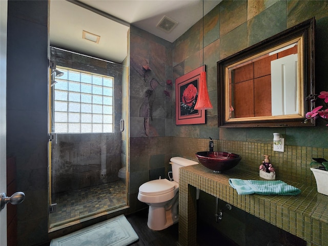 bathroom with a shower with door, vanity, tile walls, and toilet