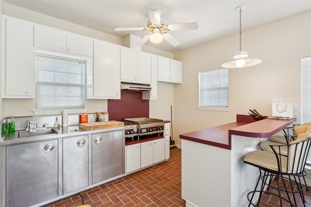 kitchen featuring a breakfast bar area, a healthy amount of sunlight, stainless steel cooktop, and decorative light fixtures