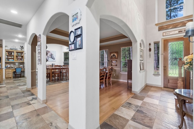 entrance foyer with crown molding, light wood-type flooring, a tray ceiling, and built in desk