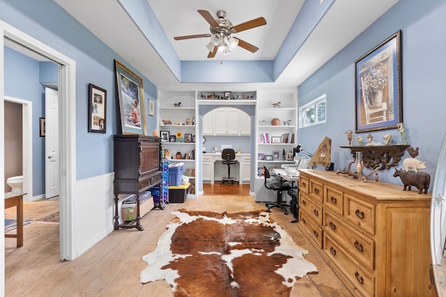 interior space featuring a raised ceiling, built in features, light hardwood / wood-style flooring, and ceiling fan