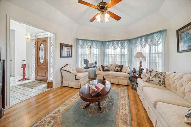 living room with light wood-type flooring, a tray ceiling, and ceiling fan