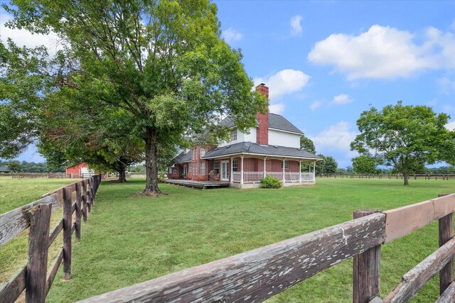 farmhouse inspired home with a wooden deck, a front lawn, and a rural view