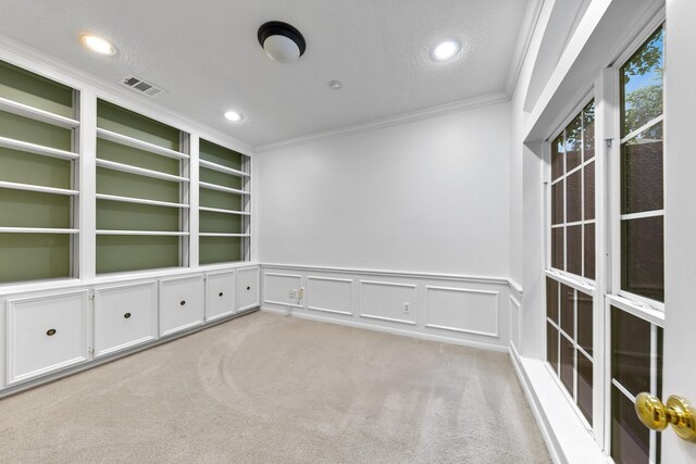 spare room with crown molding, a textured ceiling, light colored carpet, and built in shelves