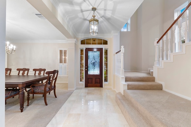 entryway with a towering ceiling, ornamental molding, light carpet, and a chandelier