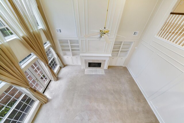 unfurnished living room featuring a towering ceiling, a premium fireplace, light colored carpet, and ceiling fan