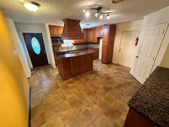 kitchen with a textured ceiling, premium range hood, tasteful backsplash, a center island, and sink