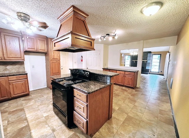 kitchen featuring dark stone countertops, black range with electric cooktop, custom range hood, ceiling fan, and a textured ceiling