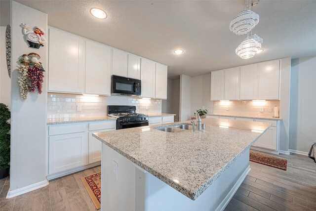 kitchen with backsplash, light hardwood / wood-style floors, white cabinetry, sink, and black appliances