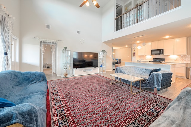 living room featuring light wood-type flooring, ceiling fan, and a towering ceiling