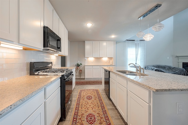 kitchen with decorative light fixtures, black appliances, sink, a center island with sink, and white cabinets