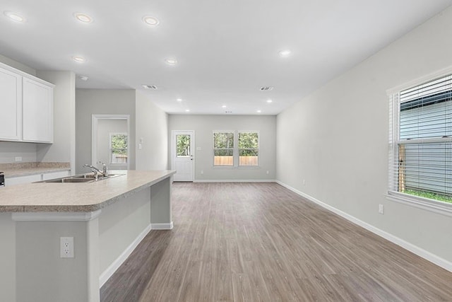 kitchen with a center island with sink, sink, hardwood / wood-style floors, and white cabinetry