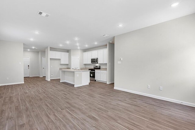 kitchen with light wood-type flooring, white cabinets, appliances with stainless steel finishes, and a kitchen island with sink