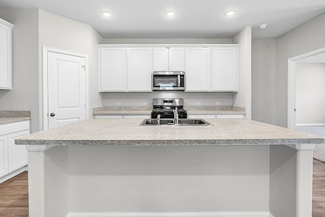 kitchen featuring dark wood-type flooring, appliances with stainless steel finishes, white cabinetry, and a kitchen island with sink