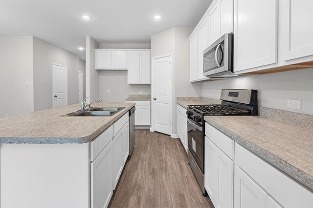 kitchen with wood-type flooring, appliances with stainless steel finishes, an island with sink, sink, and white cabinets