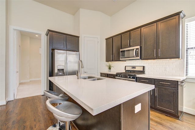 kitchen with light wood finished floors, stainless steel appliances, tasteful backsplash, a sink, and dark brown cabinetry