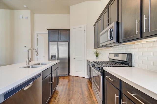 kitchen with light countertops, backsplash, appliances with stainless steel finishes, dark wood-type flooring, and a sink