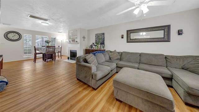 living room with ceiling fan, light hardwood / wood-style floors, and a textured ceiling