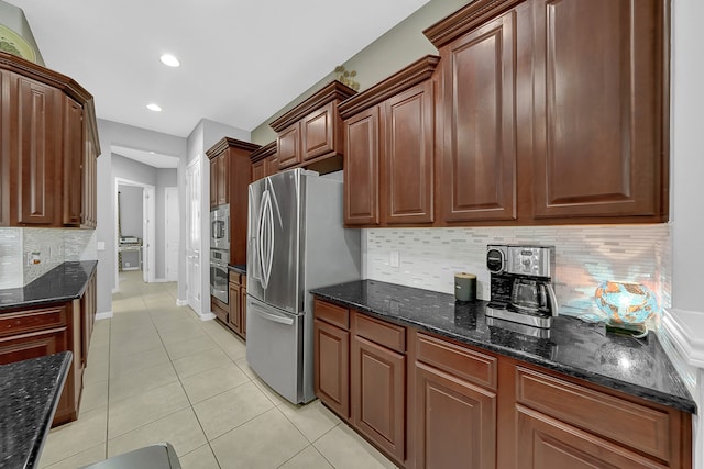 kitchen featuring appliances with stainless steel finishes, light tile patterned floors, dark stone counters, and decorative backsplash