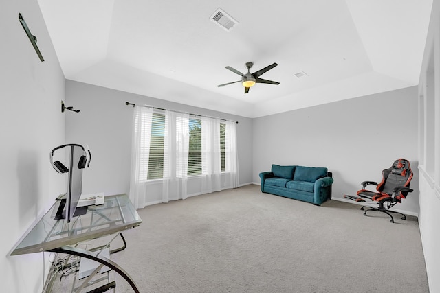 living area with a tray ceiling, light colored carpet, and ceiling fan