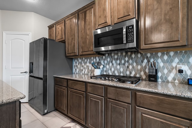 kitchen with stainless steel appliances, light tile patterned flooring, decorative backsplash, and light stone counters