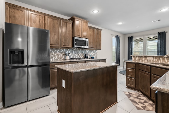 kitchen featuring decorative backsplash, light tile patterned floors, a kitchen island, light stone countertops, and appliances with stainless steel finishes