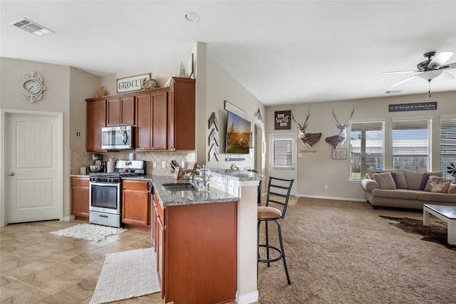 kitchen featuring tasteful backsplash, ceiling fan, appliances with stainless steel finishes, light stone countertops, and sink