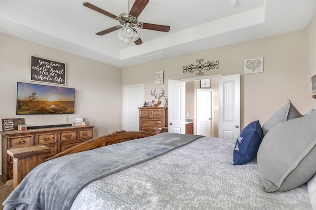 bedroom with connected bathroom, ceiling fan, and a raised ceiling