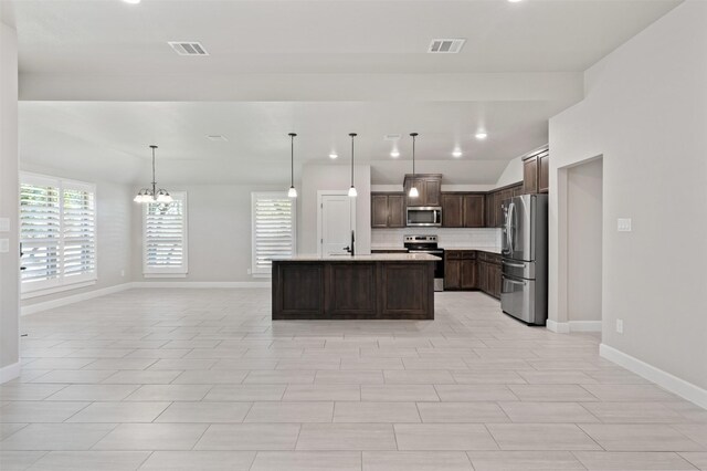 kitchen featuring appliances with stainless steel finishes, pendant lighting, an island with sink, and a notable chandelier