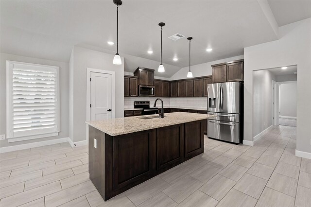 kitchen featuring a kitchen island with sink, backsplash, stainless steel appliances, sink, and light stone countertops