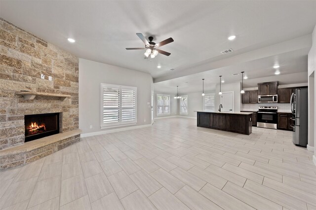 kitchen with a fireplace, decorative light fixtures, stainless steel appliances, an island with sink, and ceiling fan