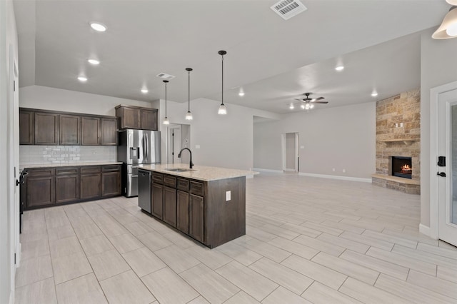 kitchen with stainless steel appliances, dark brown cabinetry, a stone fireplace, and tasteful backsplash