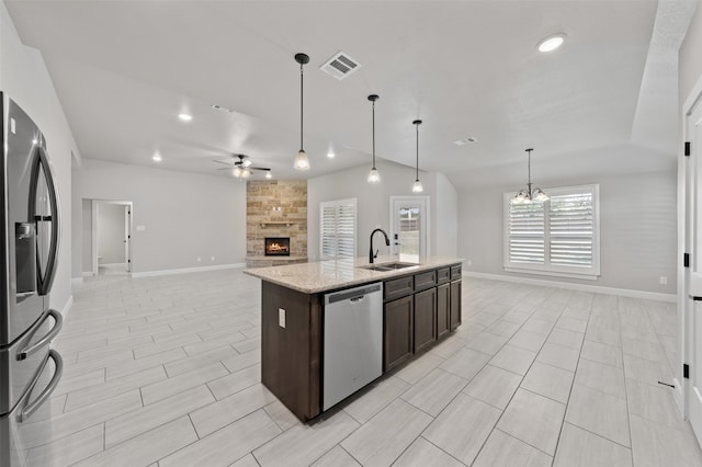 kitchen with a fireplace, ceiling fan with notable chandelier, appliances with stainless steel finishes, sink, and an island with sink