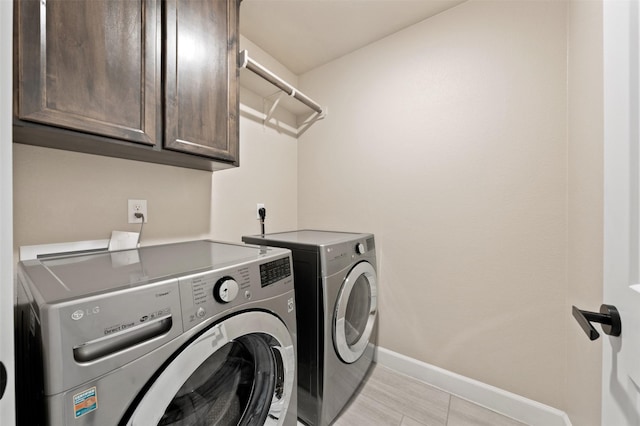 clothes washing area featuring washer and dryer, cabinet space, and baseboards