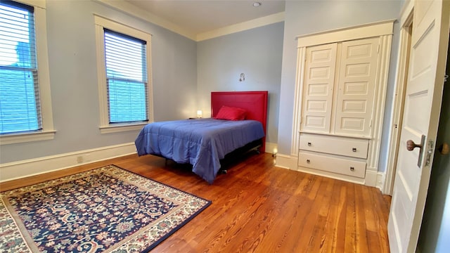 bedroom with hardwood / wood-style flooring, a closet, crown molding, and multiple windows