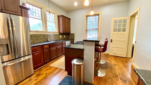 kitchen featuring appliances with stainless steel finishes, tasteful backsplash, sink, pendant lighting, and light hardwood / wood-style flooring