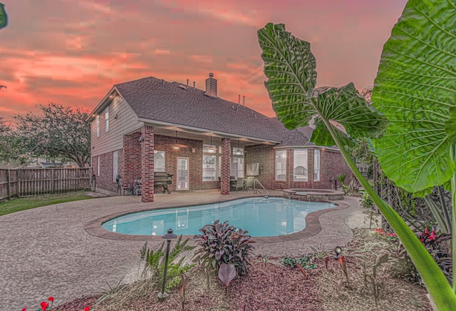 pool at dusk with an in ground hot tub and a patio