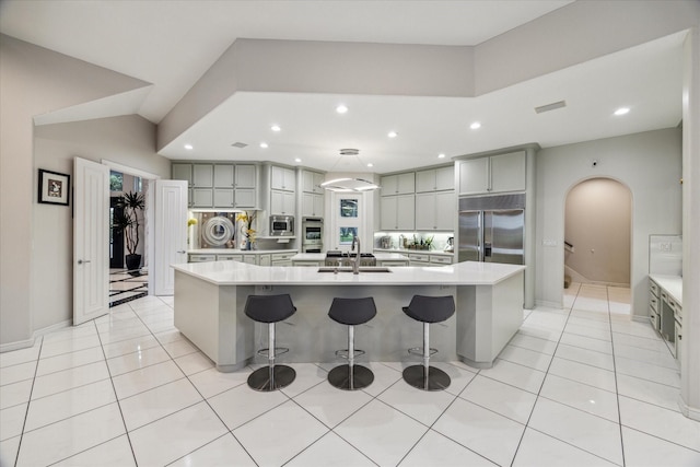 kitchen featuring built in appliances, gray cabinets, a sink, and a large island with sink