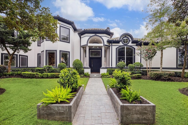 view of front of property with a tiled roof, a front lawn, and stucco siding