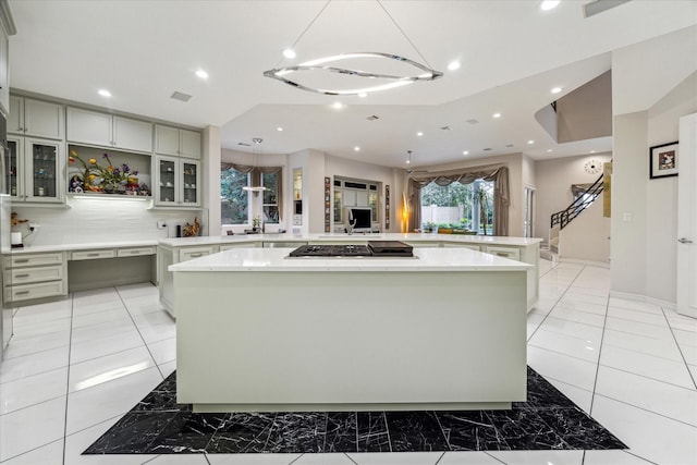 kitchen featuring stainless steel gas cooktop, a spacious island, recessed lighting, light countertops, and glass insert cabinets