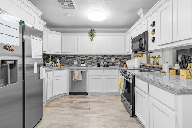 kitchen featuring light wood-type flooring, ornamental molding, white cabinetry, stainless steel appliances, and light stone counters