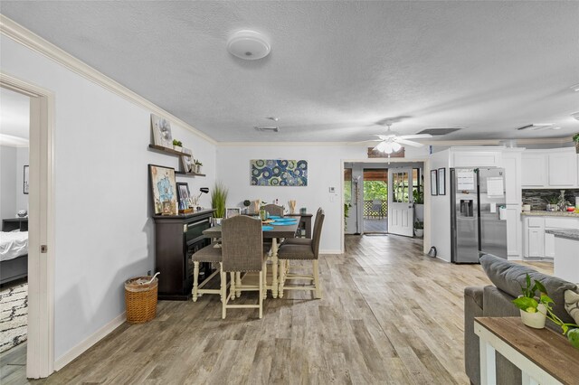 dining area featuring light wood-type flooring, ceiling fan, ornamental molding, and a textured ceiling