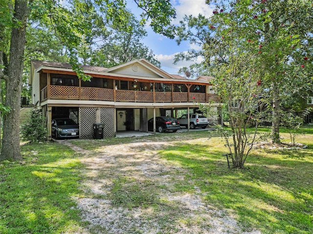 rear view of house featuring a carport, a sunroom, dirt driveway, and a lawn