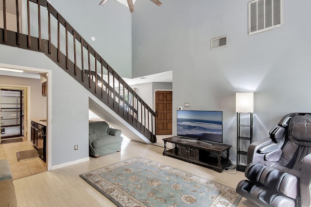 living room featuring a towering ceiling, ceiling fan, and light hardwood / wood-style floors