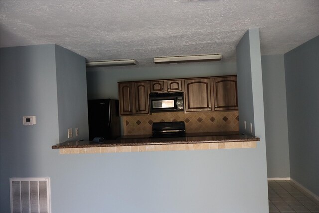 kitchen featuring black appliances, decorative backsplash, light tile patterned flooring, and a textured ceiling