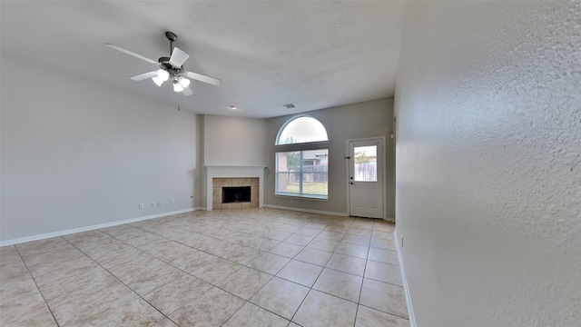 unfurnished living room featuring ceiling fan, a tile fireplace, and light tile patterned flooring